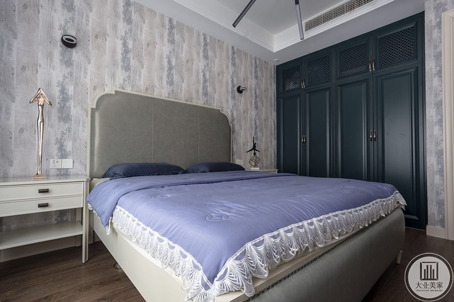 一楼次卧，背景墙使用了定制壁纸，纹理较为复杂与顶面形成对比。次卧用做了内嵌式的衣柜，柜门是较为深的蓝色。床头柜就比较简单，整个空间简繁有度，颜色搭配非常自然和谐。