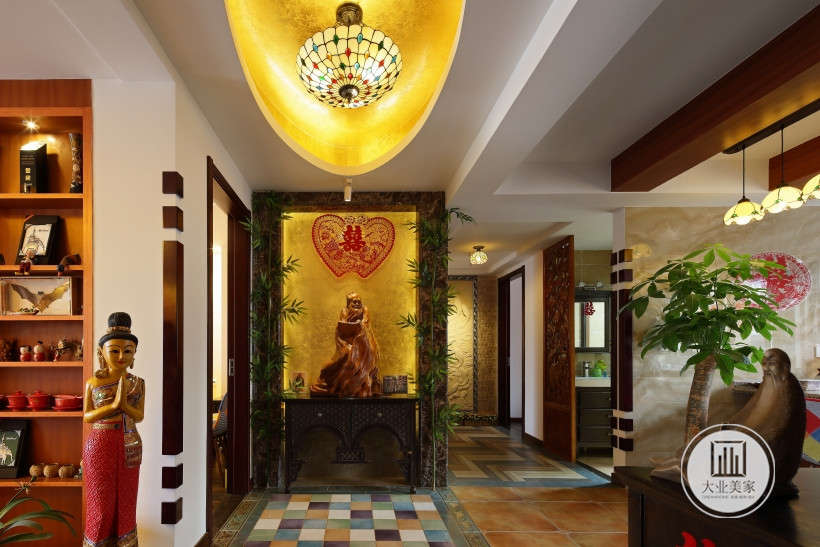 入户黑色木柜摆放木佛像和喜帖装饰，左侧客厅处东南亚人物形象雕塑摆放。地面蓝黄相间的面包砖和面包砖铺设，营造西域风情效果。